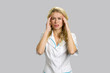 Young blond nurse having headache. Unhappy young nurse or female doctor keeping her hands on cheekbones over grey background.