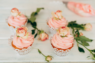 Delicate tasty muffins with a pink cream decorated with real roses on a wooden background