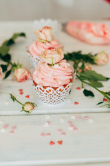 Delicate tasty muffins with a pink cream decorated with real roses on a wooden background