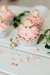 Delicate tasty muffins with a pink cream decorated with real roses on a wooden background