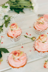 Delicate tasty muffins with a pink cream decorated with real roses on a wooden background