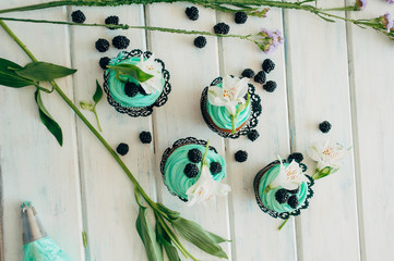 Delicate tasty muffins with mint cream decorated with fresh blackberries and orchid flowers on a wooden background.