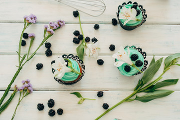 Delicate tasty muffins with mint cream decorated with fresh blackberries and orchid flowers on a wooden background.