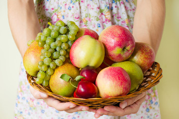 Fresh ripe fruit on a wicker wooden plate in the hands of a young woman.  Autumn harvest of fruits.