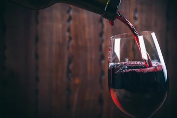 Keuken foto achterwand Wijn Rode wijn gieten in het glas tegen houten achtergrond