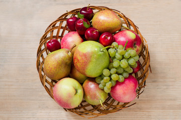 Fresh ripe fruit - apples, pears, grapes and plums in a wicker wooden plate on a wooden table. View from above. Autumn harvest of fruits. Copy Space