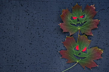 Dark halloween background - a face on an autumn maple leaf with red eyes. Copy space