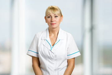 Portrait of nurse in white uniform. Medical doctor woman standing on blurred background.