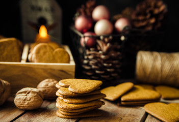 Home baked Christmas gingerbread pepper cookies stacked, in wood box. Colorful baubles, pine cones in basket. Lit candle with angel figure, festive atmosphere.