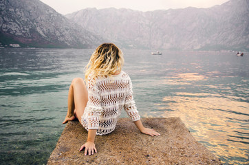 Beautiful young blonde sitting on concrete dock and enjoying the view, back view 