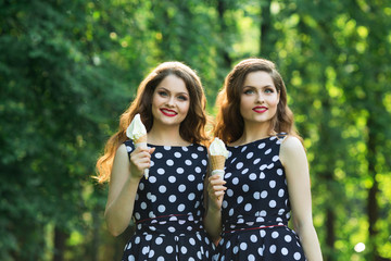 Fototapeta premium Two girlfriends sister twins of the same appearance with makeup and hairdo in the summer park eating ice cream