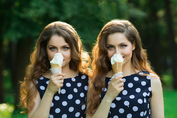 Two girlfriends sister twins of the same appearance with makeup and hairdo in the summer park eating ice cream