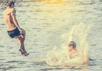 Boys falling jumping into the water with big splash. Toned image.