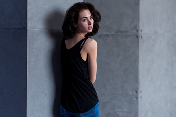 Slim young brunette turning head looking back standing at wall