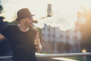 Modern happy young man in hat with a beard fun Vaporizers, In the background, the evening sunset...