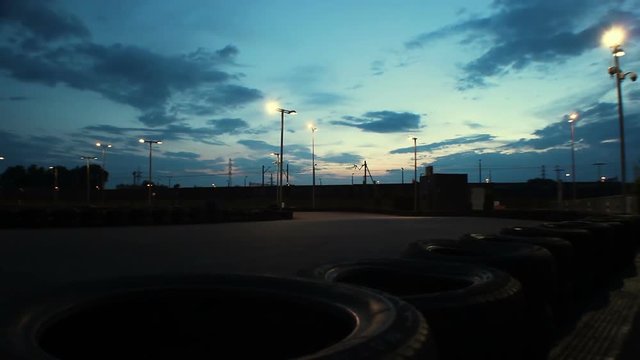 Outdoor go-kart track with cars passing under dark blue evening sky, time-lapse 
