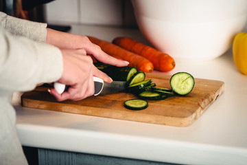 Beautiful woman in cutting cucumber on kitchen board.