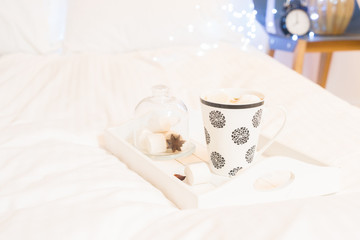 Fototapeta na wymiar Breakfast in bed - wooden tray with cup of coffee and marshmallows, cozy hygge home style