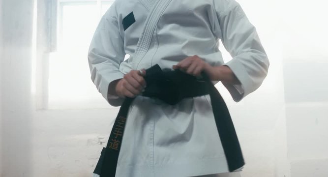 CU female karate fighter tightens the black belt on her kimono before training. 4K UHD, 60 FPS SLO MO