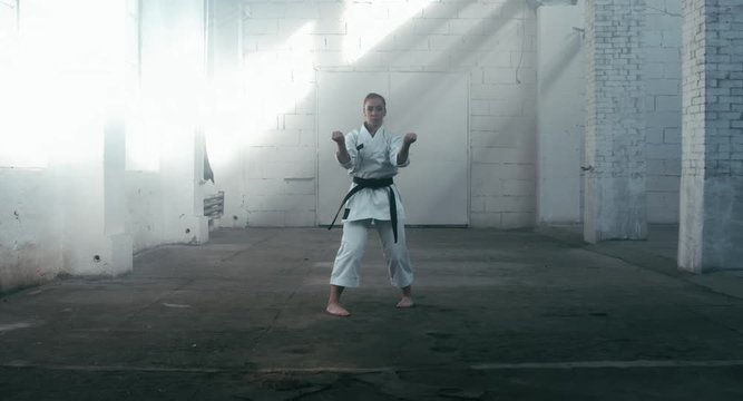 MED Caucasian professional female athlete wearing kimono practicing karate in abandoned warehouse, DX shot. 4K UHD, 60 FPS SLO MO