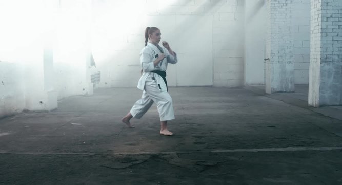 MED Caucasian professional female athlete wearing kimono practicing karate in abandoned warehouse, DX shot. 4K UHD, 60 FPS SLO MO