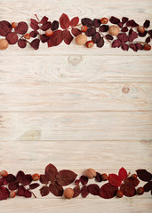 Flat lay frame of autumn crimson leaves, hazelnuts and walnuts on a light wooden background.