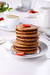 Stack of chocolate pancakes with strawberries on white wooden table. Breakfast.