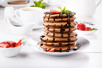 Stack of chocolate pancakes with chocolate topping and strawberries