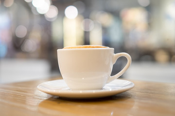 A cup of cappuccino coffee on wooden table in the background of cafeteria