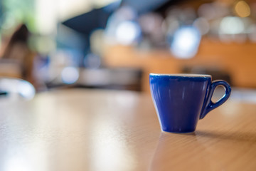 A blue cup of espresso coffee on wooden table in the background of cafeteria