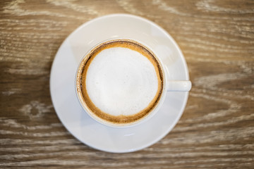 A cup of cappuccino coffee on wooden table in the background of cafeteria