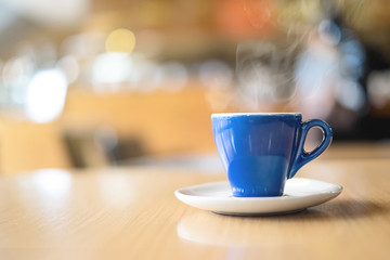 A blue cup of espresso coffee on wooden table in the background of cafeteria