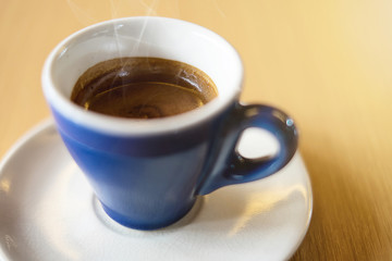 A blue cup of espresso coffee on wooden table in the background of cafeteria
