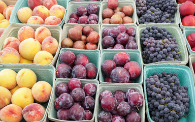 Assorted fruit at a Farmer's Market Stall including, ripe peaches, purple plums, and grapes