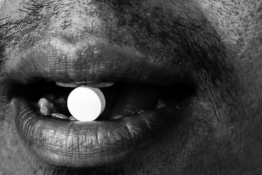 Man Taking A Tablet. Close Up Mouth With A Pill On Mouth In White Tone