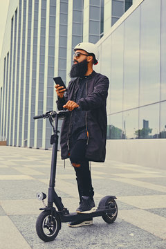 A Man Riding By Electric Scooter And Using A Smart Phone.