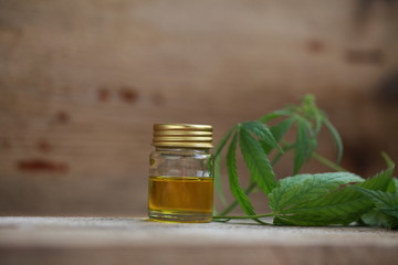 A cannabis leaf and a bottle of hemp oil on a wooden table