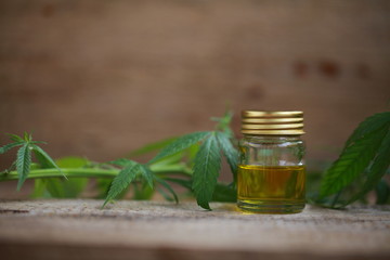 A cannabis leaf and a bottle of hemp oil on a wooden table
