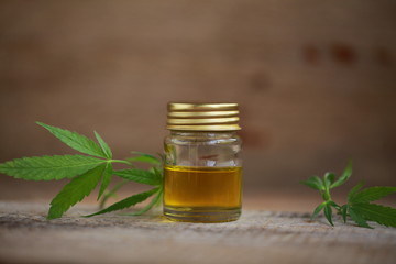 A cannabis leaf and a bottle of hemp oil on a wooden table