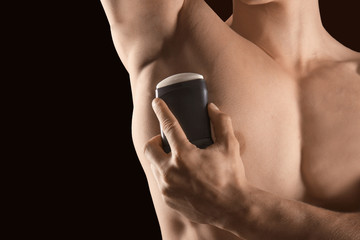 Handsome young man with deodorant on dark background