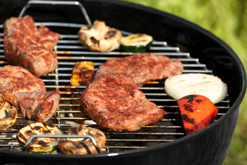 Tasty beefsteaks and vegetables cooking on barbecue grill outdoors, close up