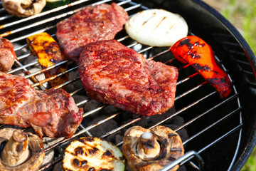 Tasty beefsteaks and vegetables cooking on barbecue grill