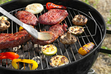 Tasty beefsteaks and vegetables cooking on barbecue grill outdoors