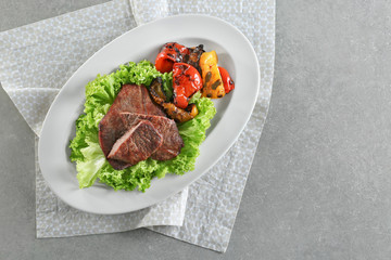 Plate with tasty grilled steaks and vegetables on grey table