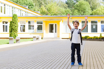 Fototapeta na wymiar Excited schoolboy with hands up near the school