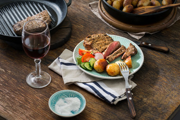 Grilled steak with potatoes, salad on wooden table with wine