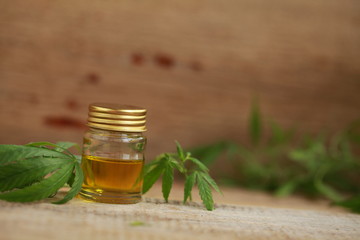 A cannabis leaf and a bottle of hemp oil on a wooden table