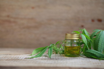 A cannabis leaf and a bottle of hemp oil on a wooden table