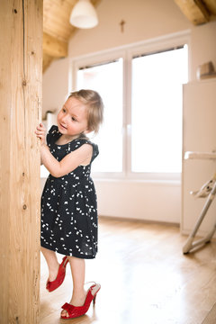 Cute little girl in dress and red high heels at home.
