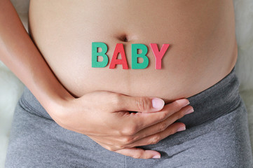 Pregnant woman with BABY word in front of her belly.